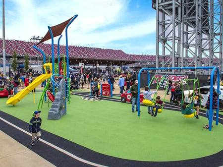 small playground on green turn with children playing on it on the side of a race car track