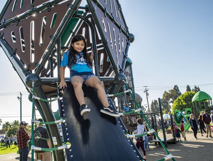 young child in blue shirt playing on a silver playground structure 