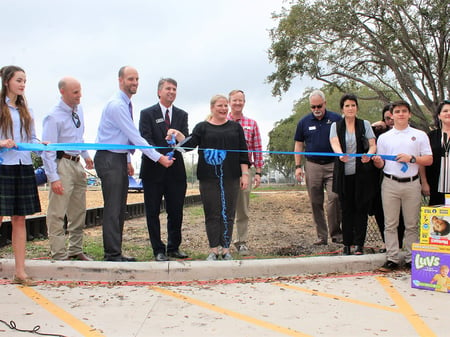 group of colleagues in business attire cutting a ribbon on a piece of land