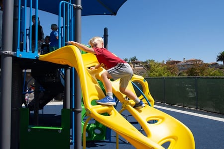 young boy in red shirt climbing up green steps at park