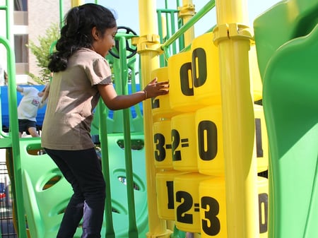 young girl with black hair in tan shirt playing with yellow spinning black numbers at park