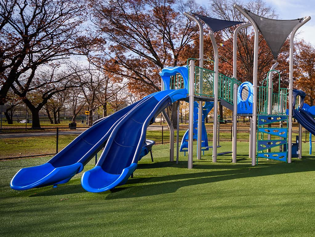 Video of blue color accent playground with kids playing on it and autumn colored trees in the background