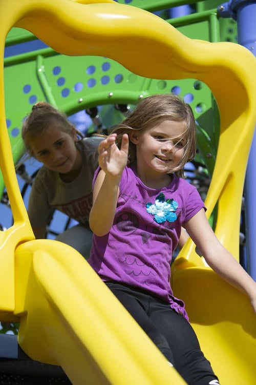 girl in purple shirt smiling on yellow slide