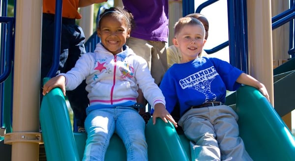 two children smiling about to go down a teal slide