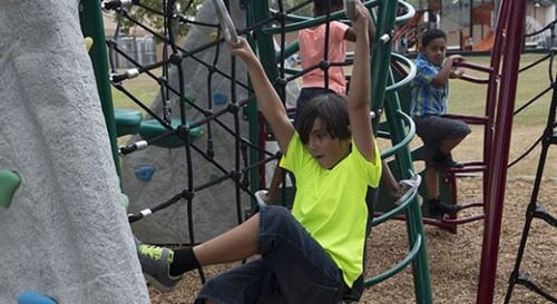 small child in light yellow shirt climbing on playground rope wall