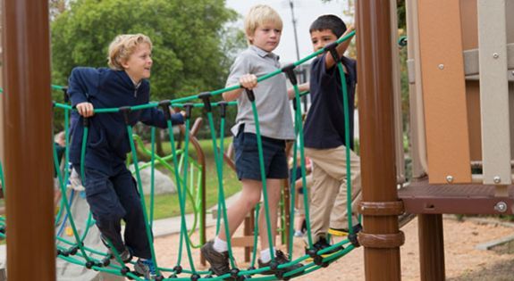 three small children playing on a bridge at a playground