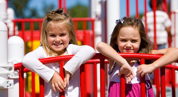 two children smiling hanging over a red rail
