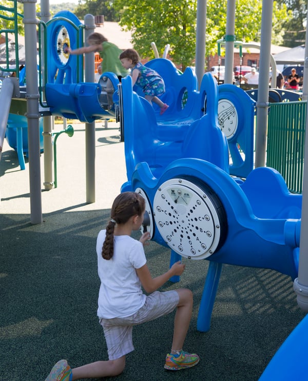 girl kneeling down playing on a blue piece of playground equipment at park