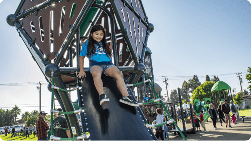 one small latino girl in blue shirt going down a black log at a park