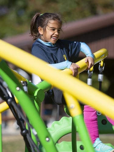child smiling and playing on a yellow and green playground bar