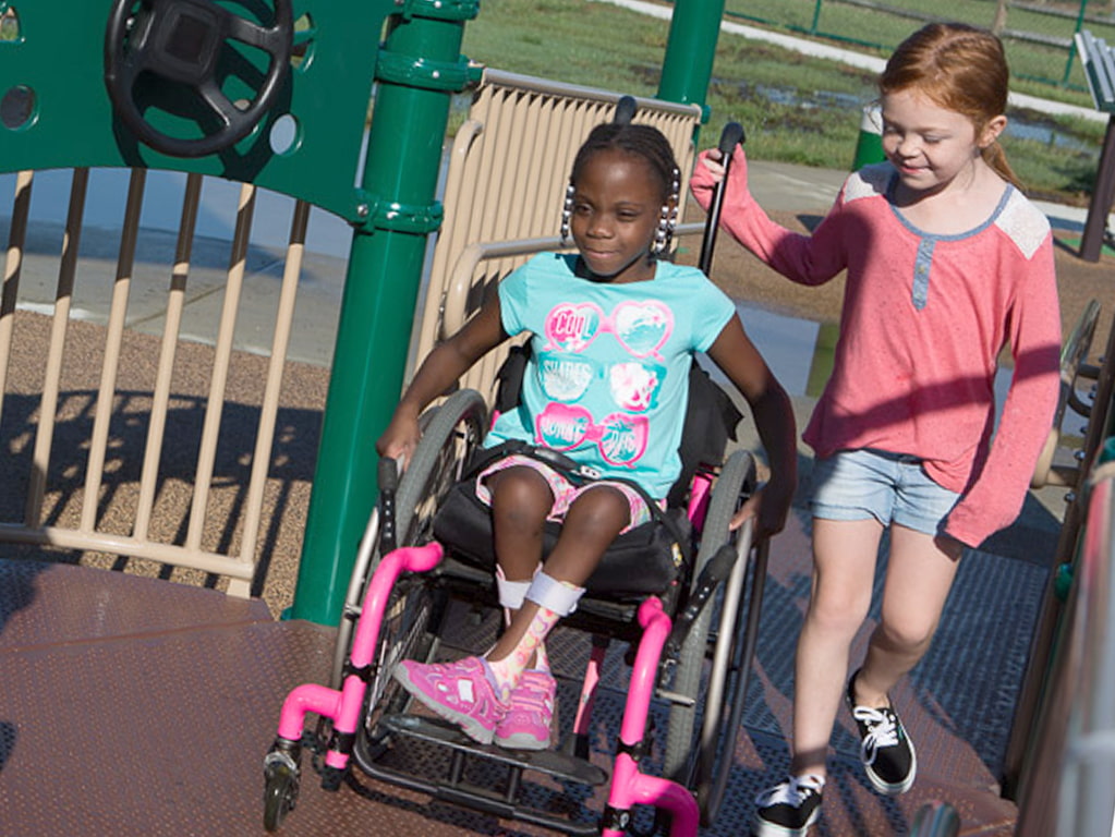 young girl in a wheelchair playing with her friend at park