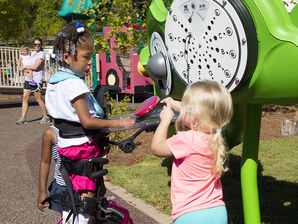 young girl with leg braces playing with her friend on playground equipment