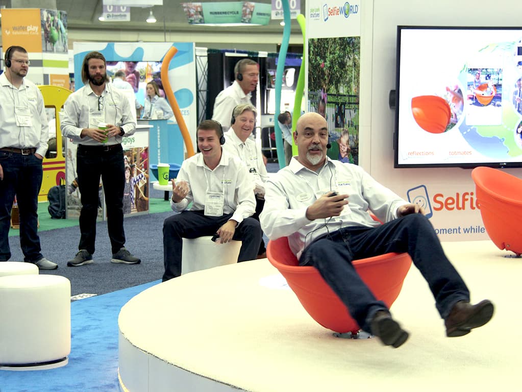 group of colleagues at a conference with one man sitting in an orange swinging playground toy model
