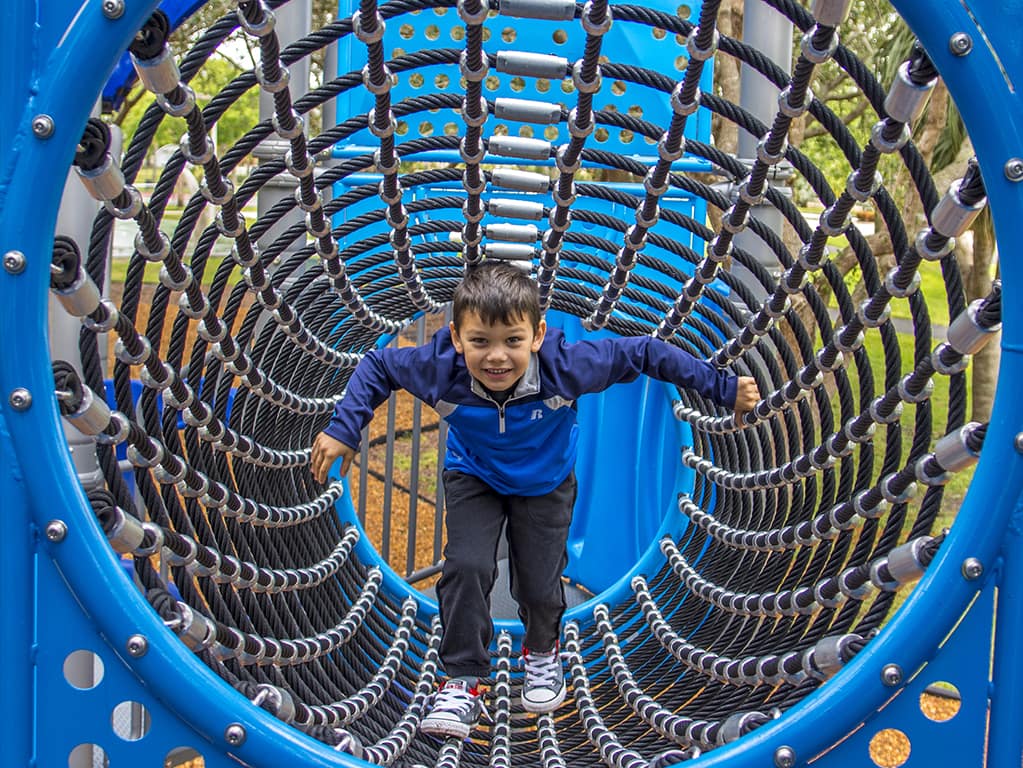 young boy in a blue jacket playing in a playground tunnel