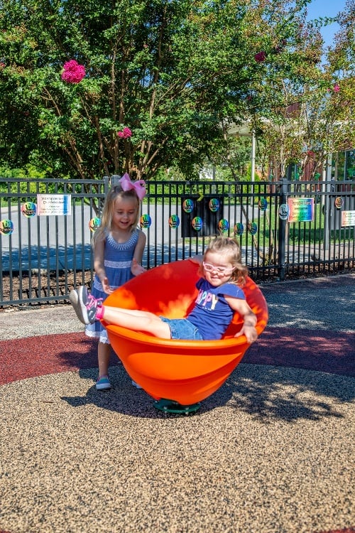 two young girls playing in a red and orange spinning playground toy