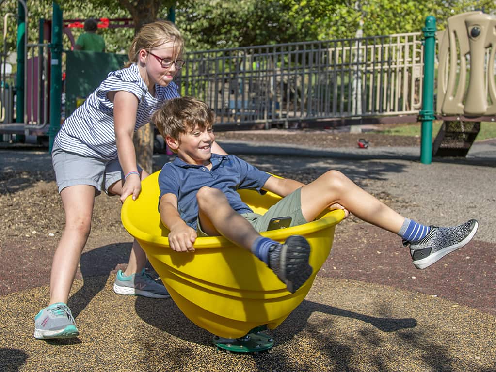 two children playing in a yellow rotating toy at park