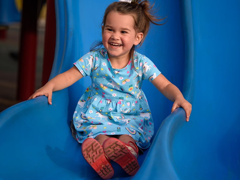 girl in light blue dress going down blue slide smiling