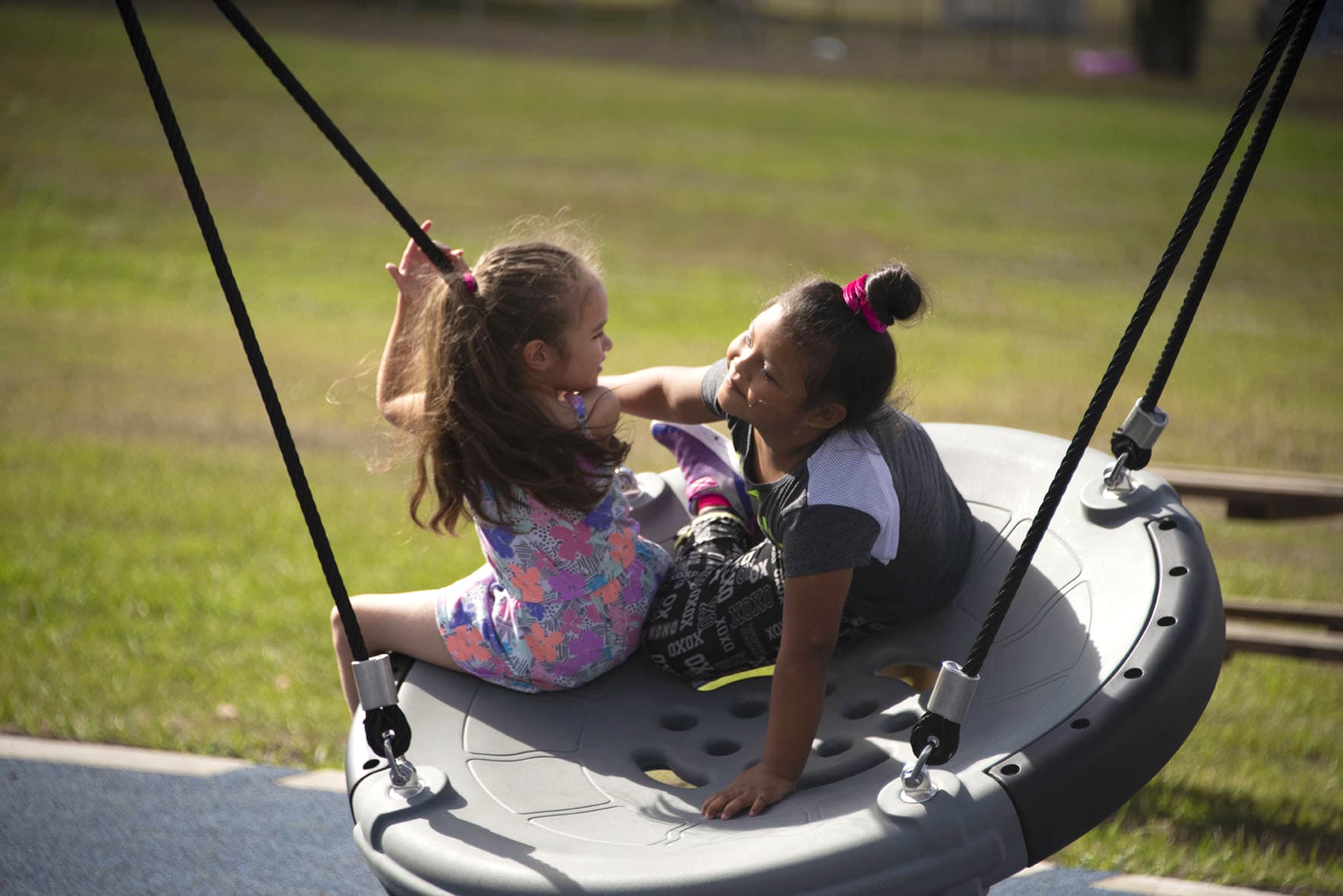 2 children playing on gray swinging playground toy