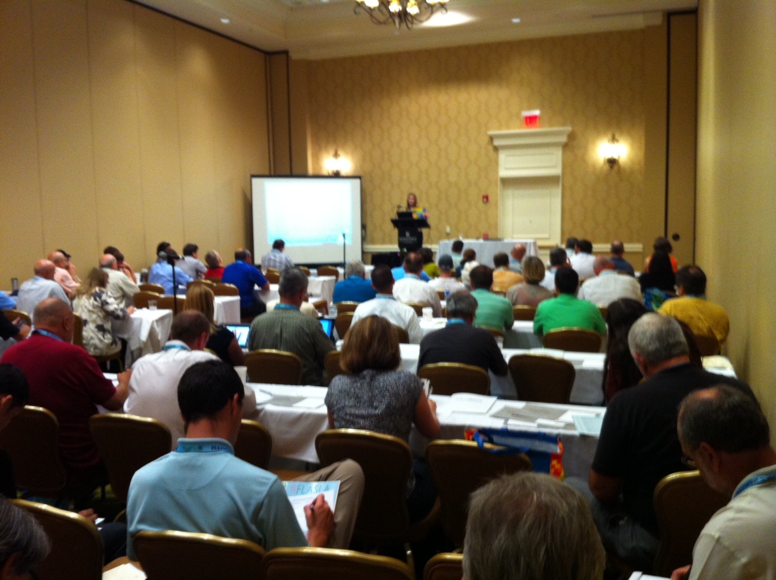 Group of people at an indoor learning session taking notes from a screen and speaker