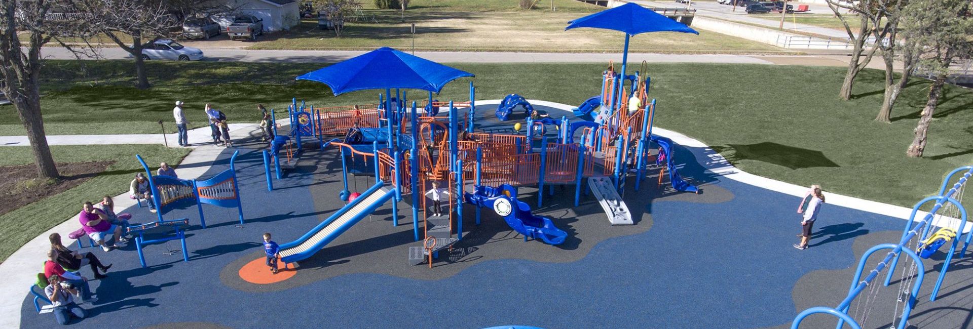 aerial shot of blue colored park on gray turf with children playing on it