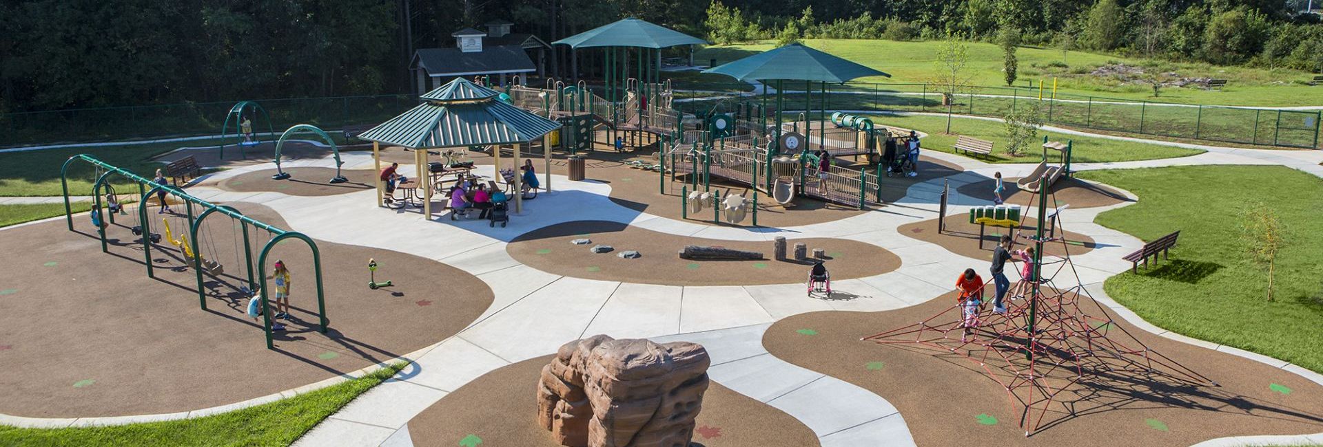 Park with teal covers, winding sidewalk throughout and patches of brown turf with children playing 