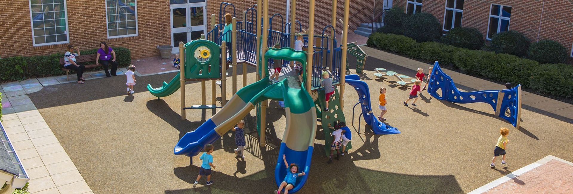 Children playing at green, blue, and tan colored park with brown turf