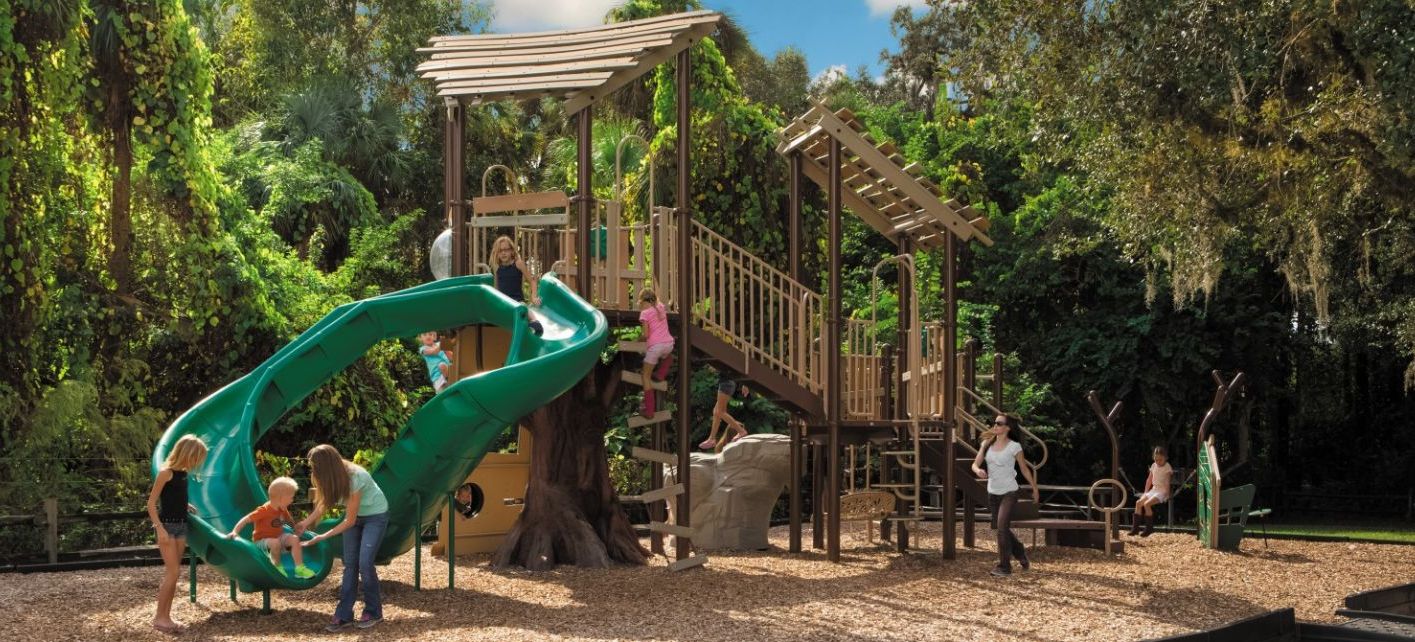 Featured image of tree house themed playground with green slide and children playing on it