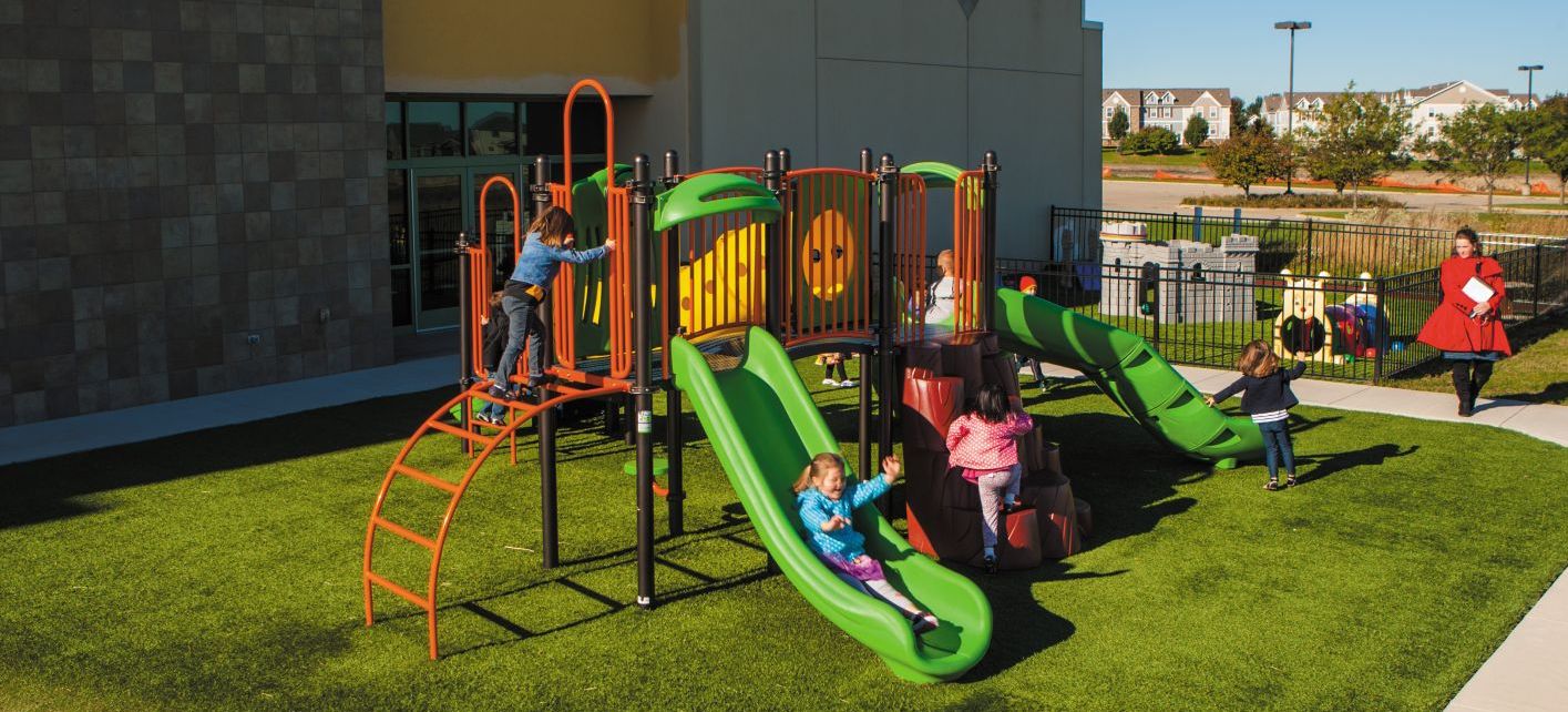 children playing at a green colored park on turf going down a green slide