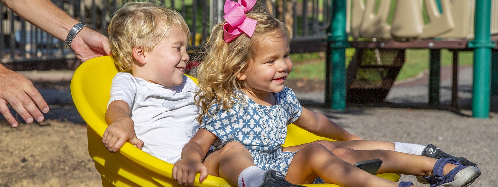 2 children smiling going down yellow slide