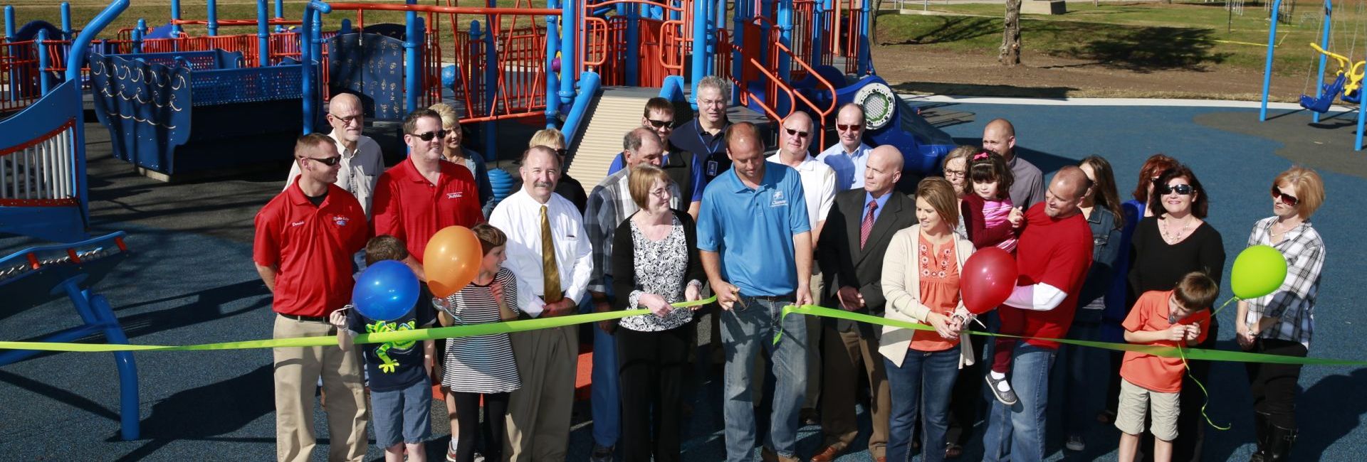 Group of people smiling cutting green ribbon at new park