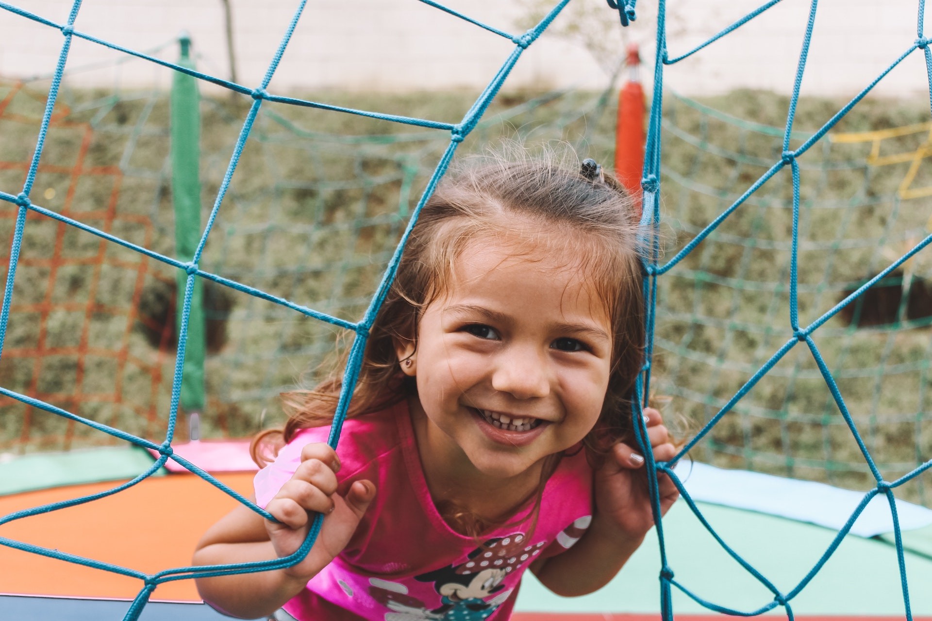 Featured image of Young girl in pink shirt poking head through net smiling 