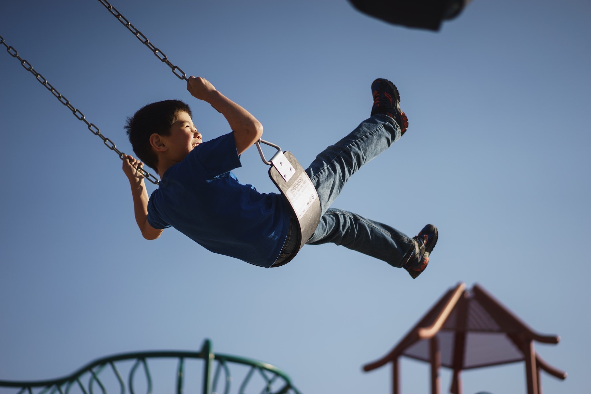 Young boy in blue shirt and jeans swinging at playground