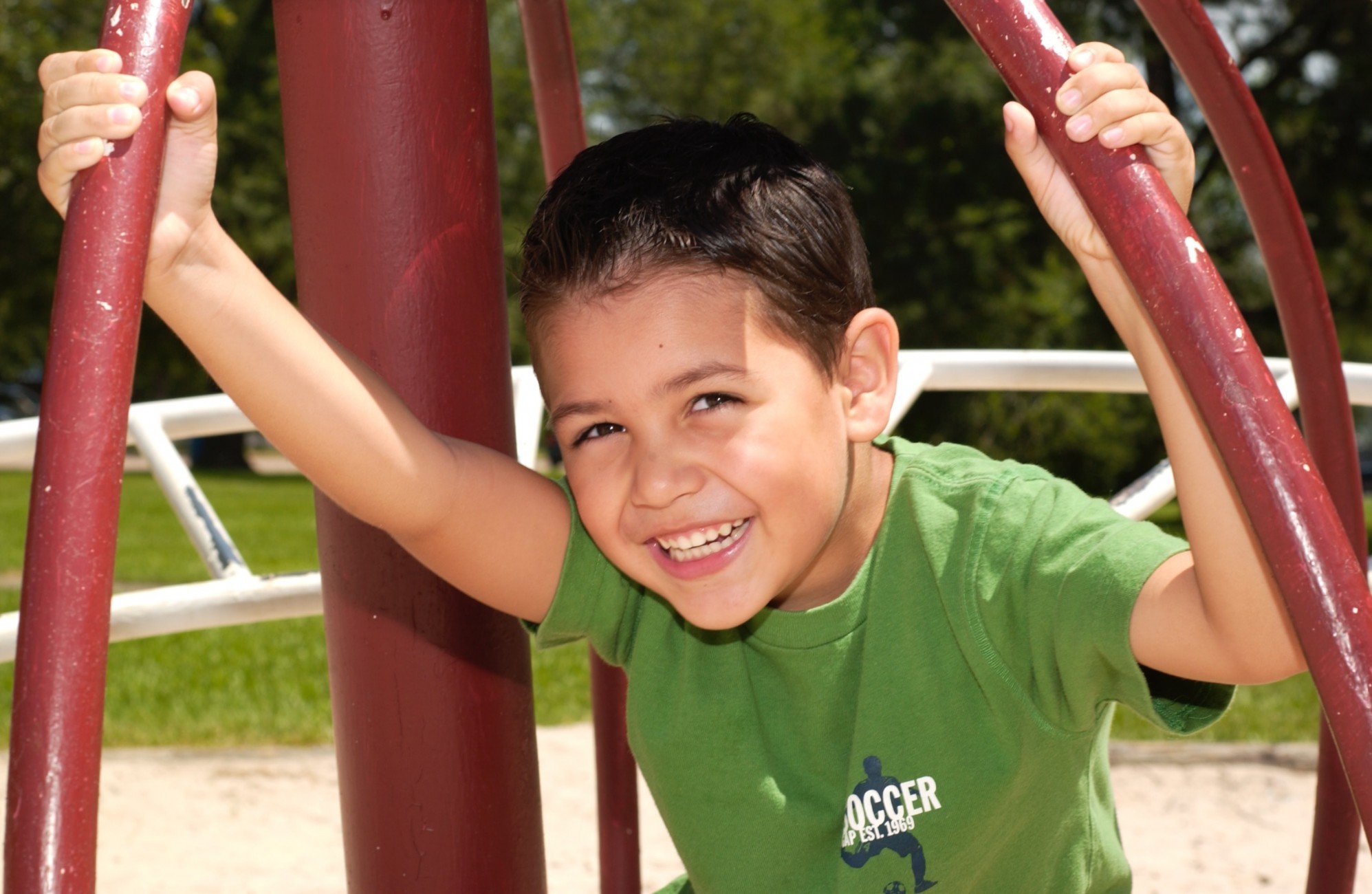 Young boy with black hair smiling at playground in green shirt