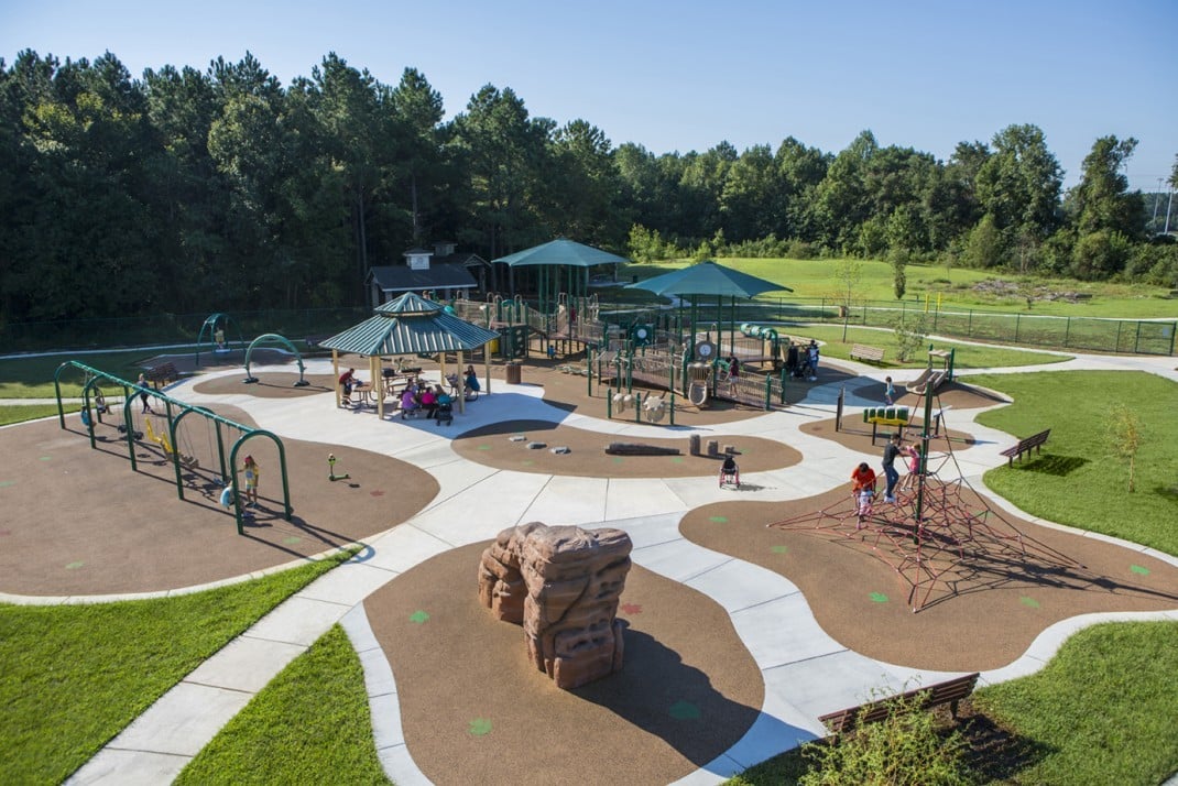 aerial view of park with green covers and brown turn with children playing on it