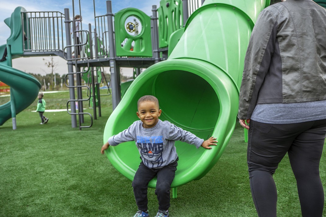 small boy smiling getting out of green slide