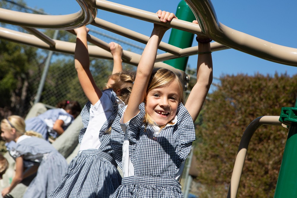 girl in black and white uniform smiling hanging on monkey bars