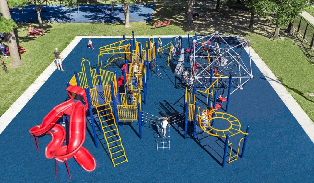 Featured image of Aerial view of playground on blue turf with red slide and children playing on it 