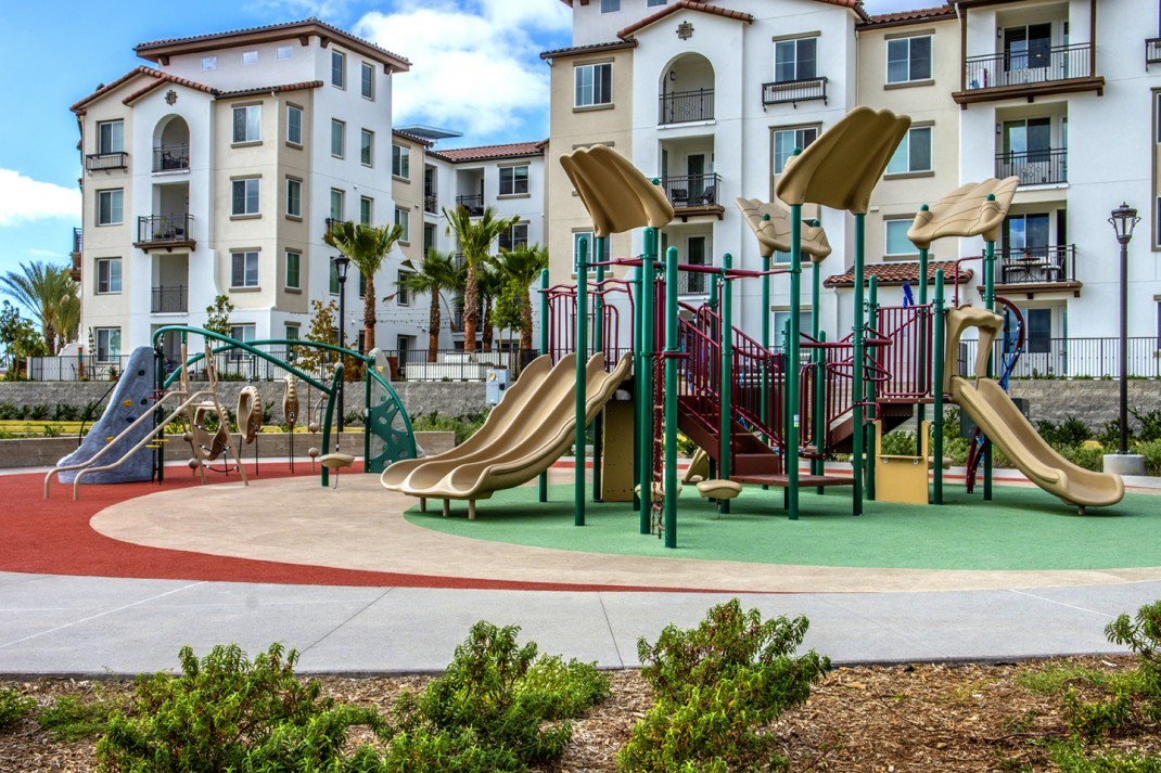 playground with tan slides in front of a nice white apartment complex