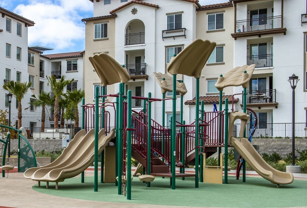 playground with tan slides in front of white apartment complex