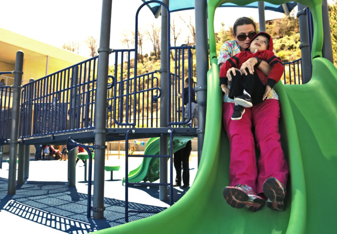 mom holding son in red jacket going down green slide