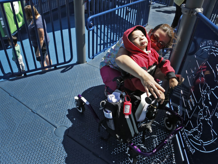 Mom helping disabled daughter in wheelchair touch object at park