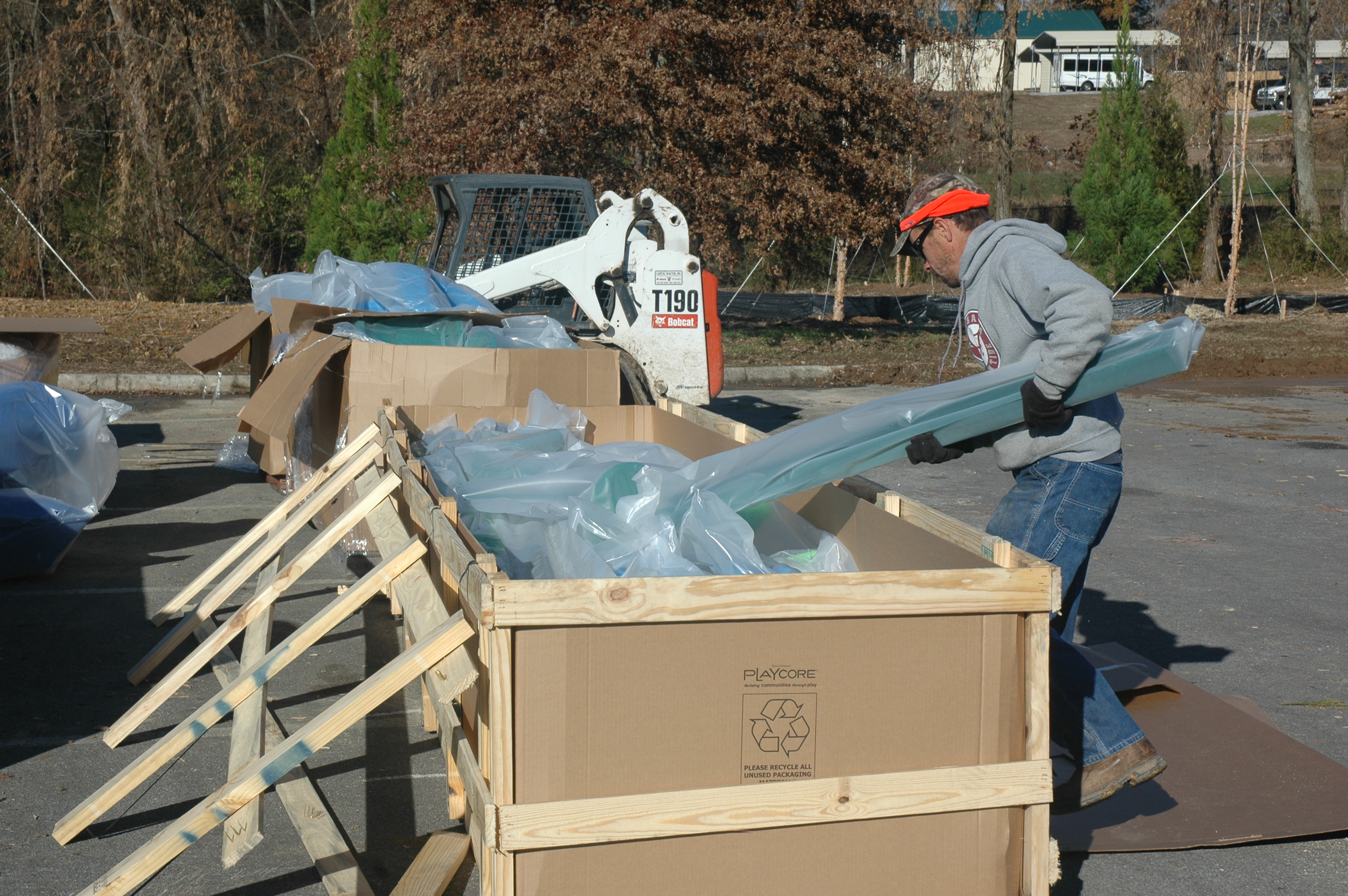 Man in grey hoodie taking bagged playground equipment out of box outside