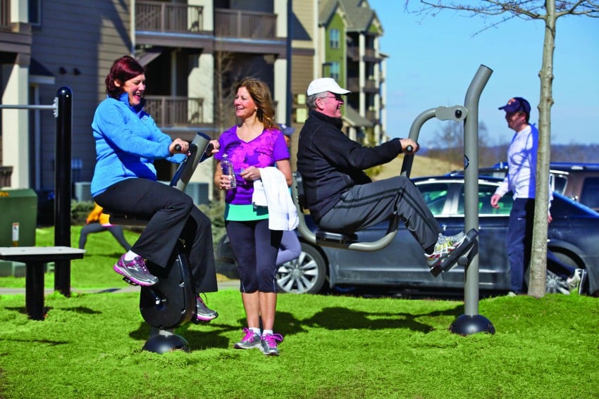 Four adults smiling, two of them on outdoor fitness equipment